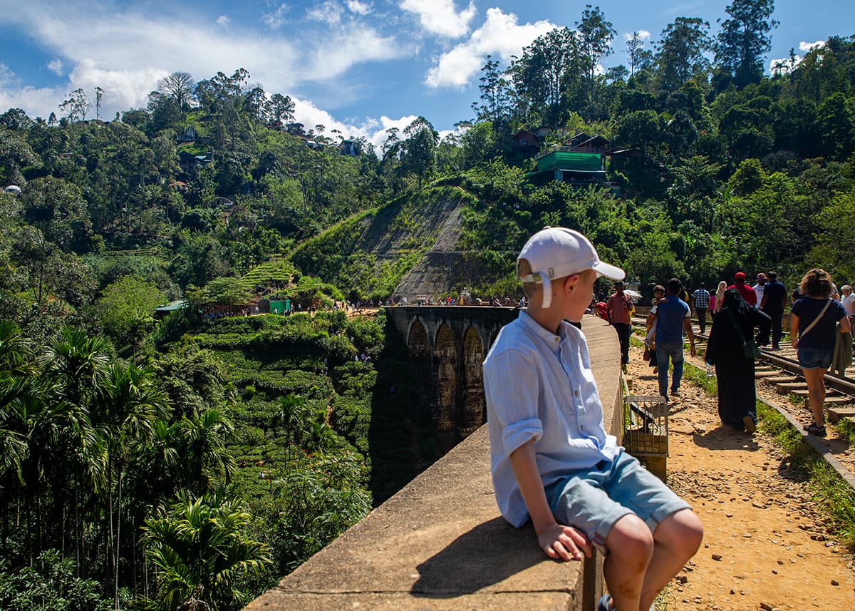 A boy sits on the edge near Nine Arches Bridge in Ella, Sri Lanka, as tourists explore the lush railway.