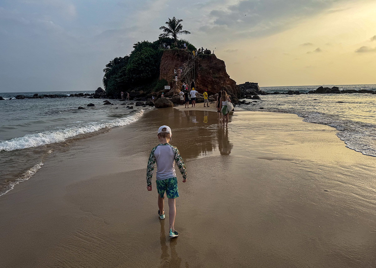 Young boy walks up to Parrot Rock at sunset in Mirissa