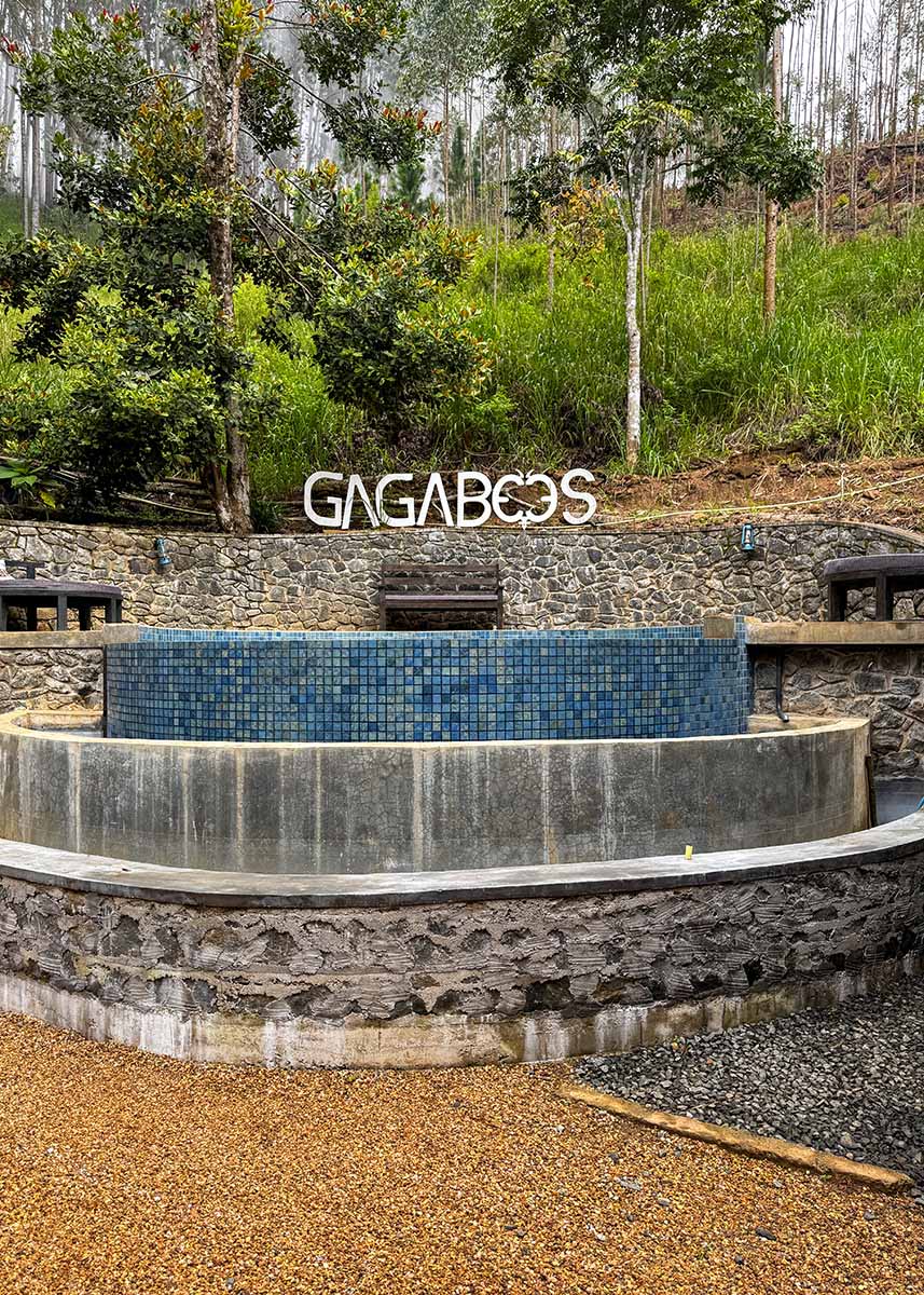 Stone and tiled pool area with “Gaga Bees” sign at eco lodge Gaga Bees Ella. Surrounded by greenery and misty hills, the setting feels calm and upscale. The weather is overcast.