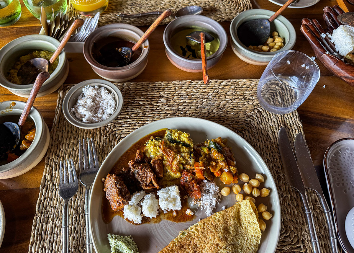 Plate of Sri Lankan rice and curry with multiple side dishes at a restaurant in Ella, Sri Lanka. Bowls of dhal, vegetables, and sambal surround the main plate. The wooden table and natural light create a warm dining setting.