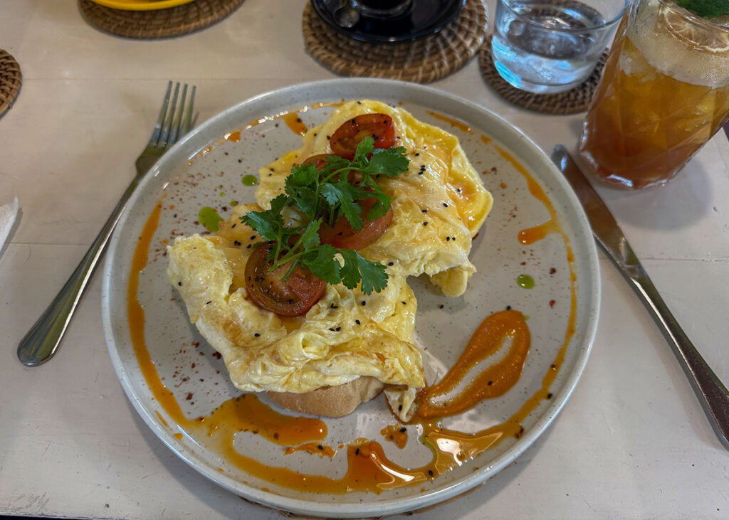 Plate of scrambled eggs with sauce and herbs on toast served with drinks at a restaurant in Negombo.