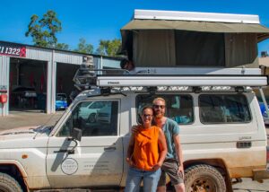 Mother and fatherstanding beside their expedition style camper vehicle in Broome, Western Australia. The rooftop tent is open and their son is peeking out of the tent.
