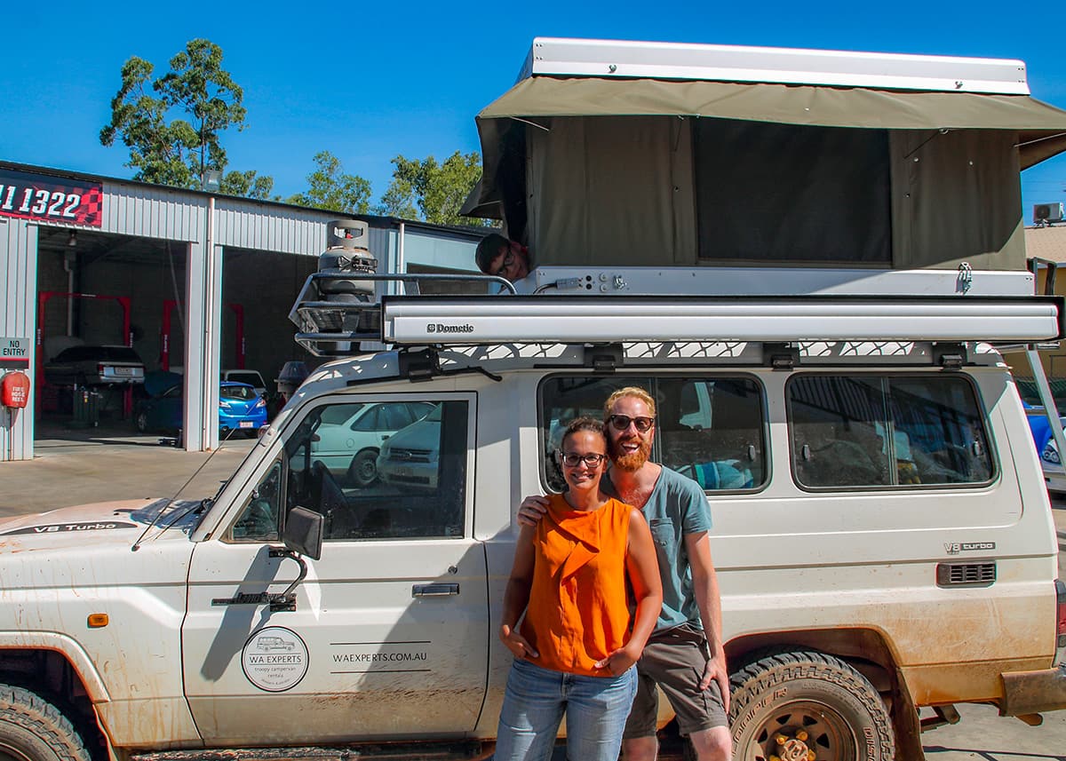 Mother and fatherstanding beside their expedition style camper vehicle in Broome, Western Australia. The rooftop tent is open and their son is peeking out of the tent.